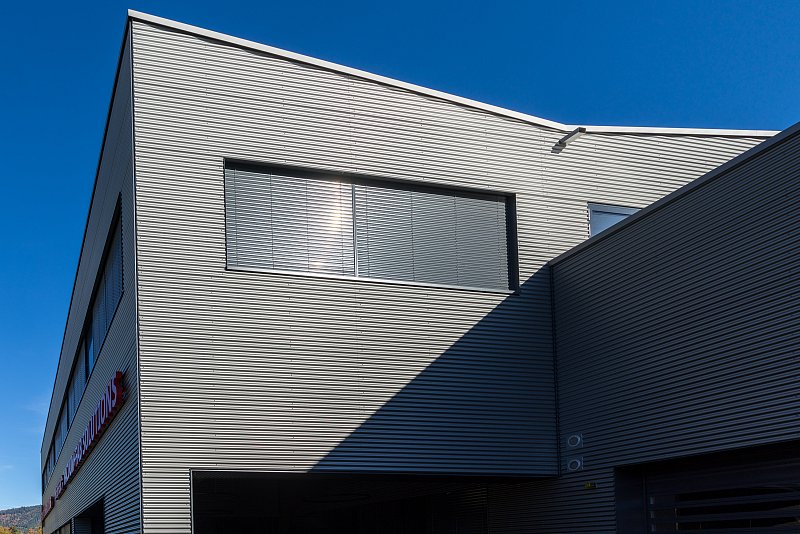 Metallfassade mit einem grossen Fenster, blauem Himmel und diagonalem Schatten.