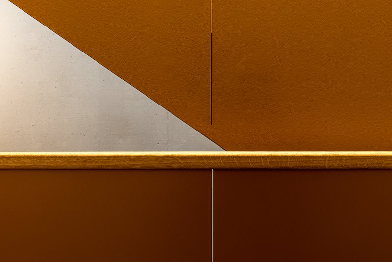Warme orange Wand und Handlauf mit einer scharf begrenzten dreieckigen Lichtfläche.