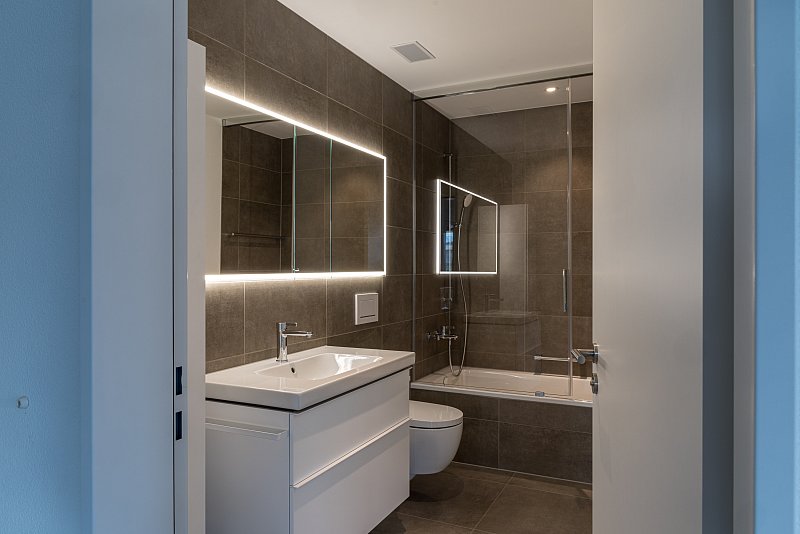 Modernes Badezimmer mit Waschtisch, beleuchtetem Spiegel und gläserner Duschabtrennung.