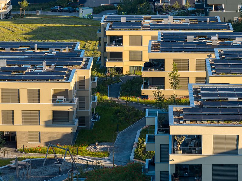 Luftaufnahme moderner Wohnhäuser mit Flachdächern und Solaranlagen.
