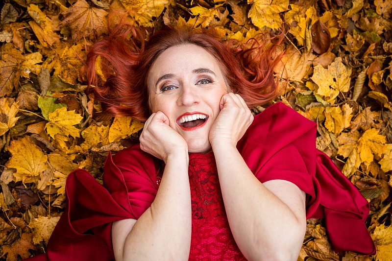 Lachende Frau in roter Kleidung auf gelbem Herbstlaub, von oben fotografiert.