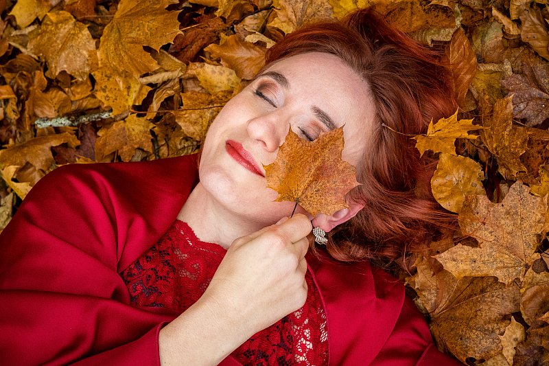 Frau mit geschlossenen Augen hält ein Herbstblatt an ihr Gesicht.