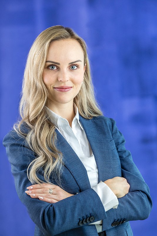 Frau im hellblauen Blazer mit verschränkten Armen vor blauem Hintergrund.